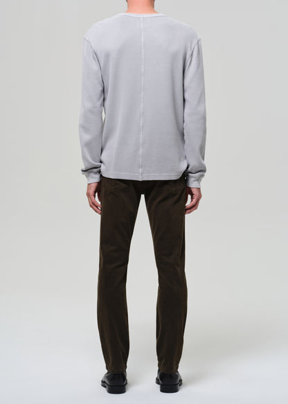 Person wearing a light gray sweater and dark brown pants on a white background