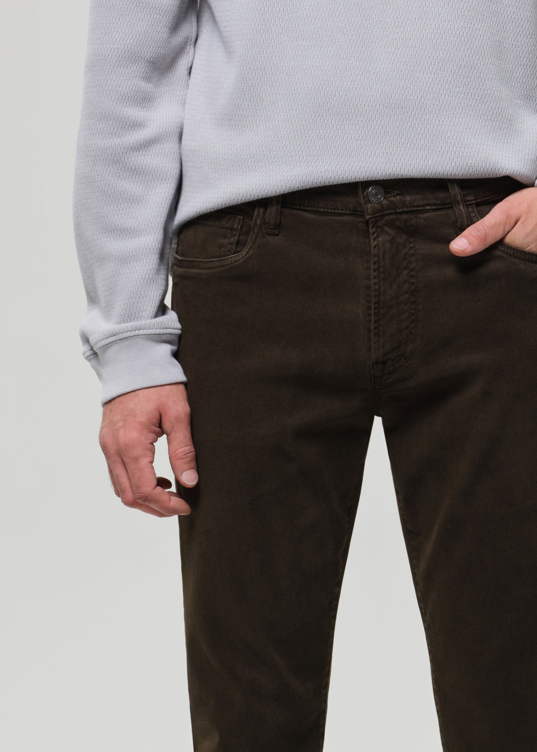 Person wearing brown pants and a light gray sweater on a plain background