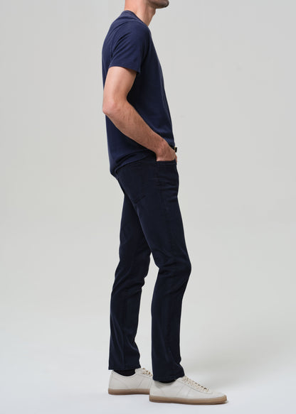 Person wearing a navy t-shirt and pants with white shoes on a light gray background