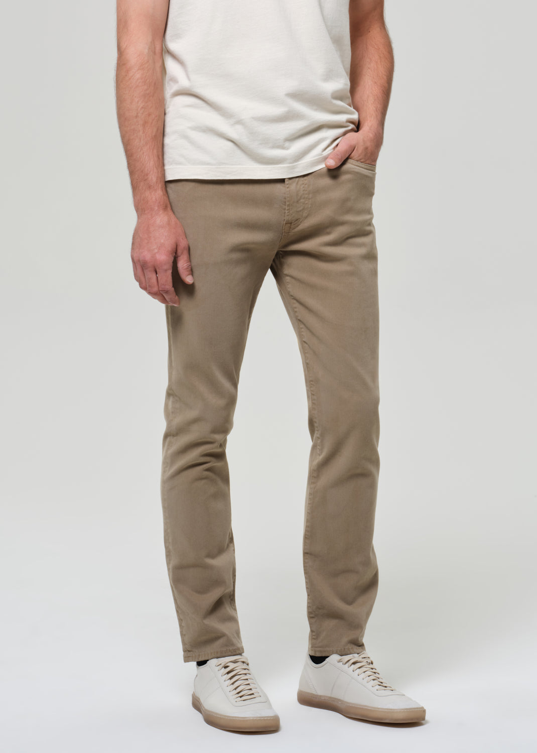Person wearing beige pants and a white shirt on a plain background