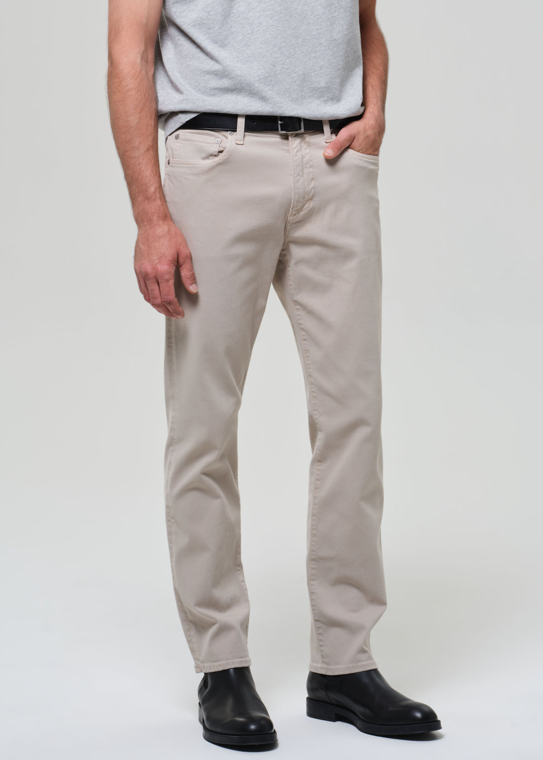 Person wearing beige pants and black shoes on a plain background
