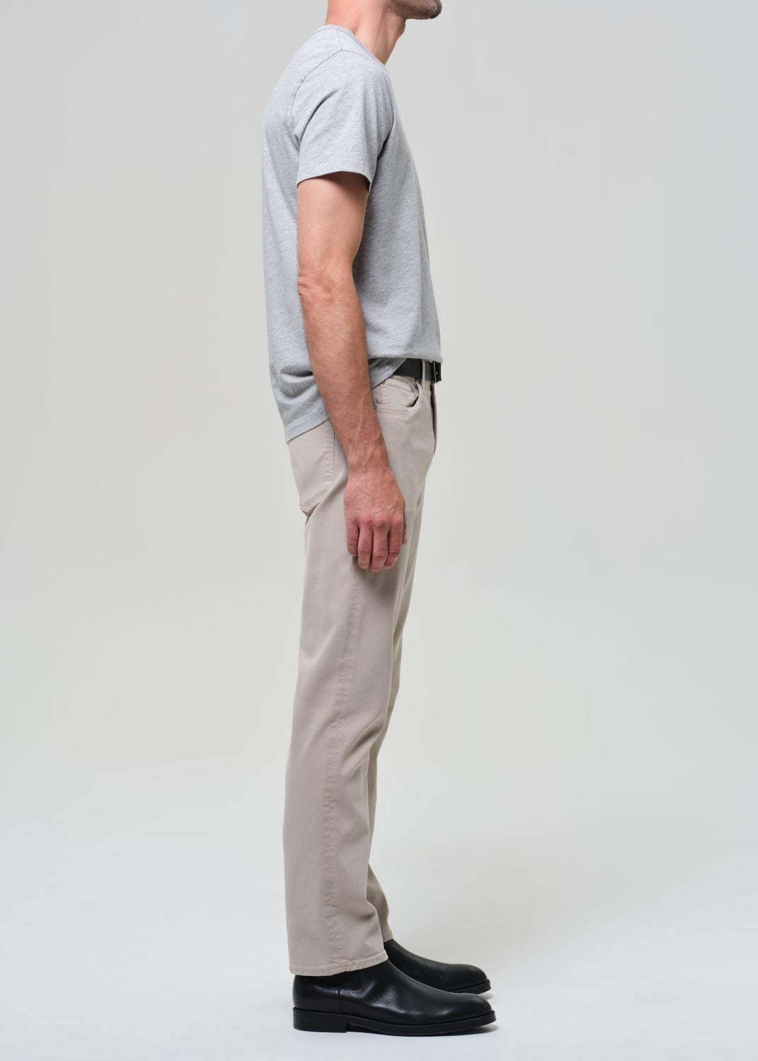 Person wearing a gray t-shirt, beige pants, and black shoes on a white background
