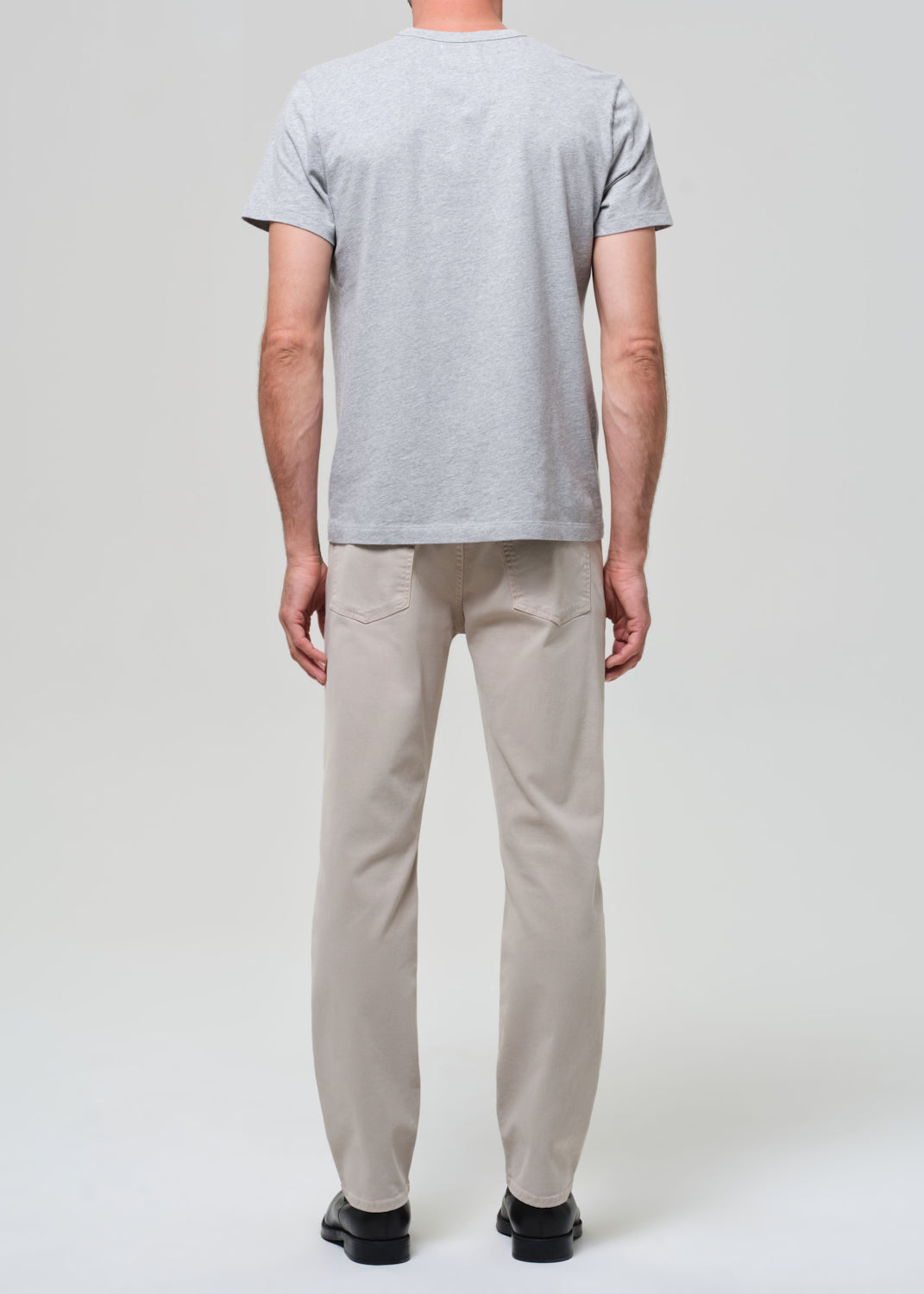 Person wearing a gray t-shirt and beige pants on a white background