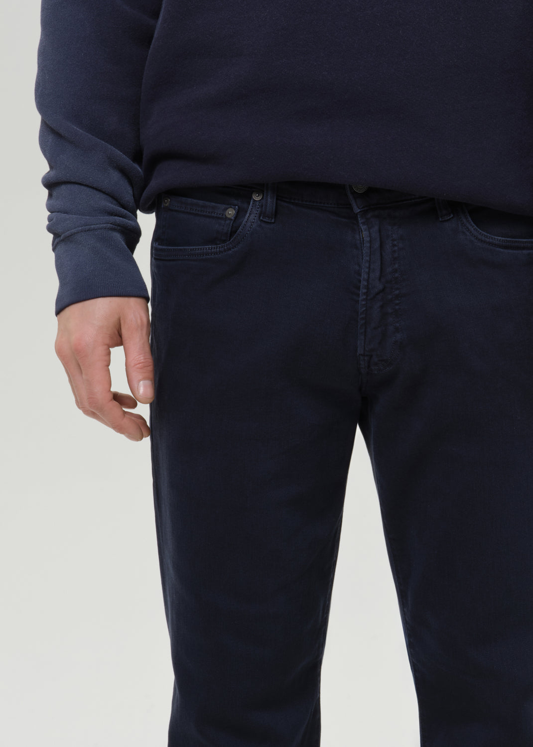 Close-up of a person wearing dark navy blue jeans and a matching navy sweatshirt against a grey background.