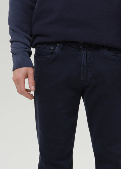 Close-up of a person wearing dark navy blue jeans and a matching navy sweatshirt against a grey background.