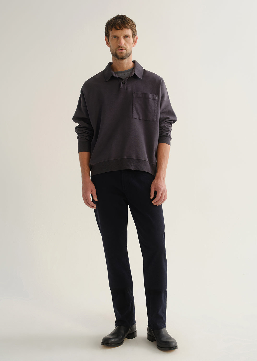 Person wearing dark navy straight leg jeans with a charcoal long sleeve shirt and black boots, front full body view on a light grey background.