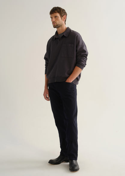 Person wearing dark navy straight leg jeans with a charcoal long sleeve shirt and black boots, angled front full body view on a light grey background.