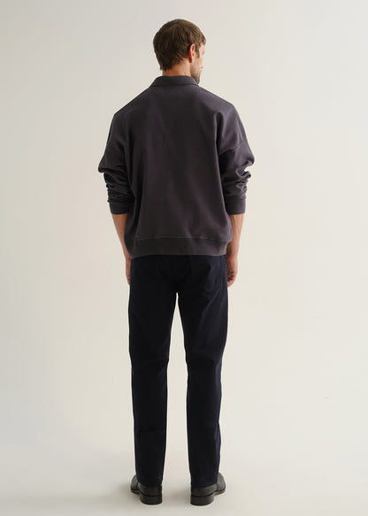 Person wearing dark navy straight leg jeans with a charcoal long sleeve shirt and black boots, back full body view on a light grey background.