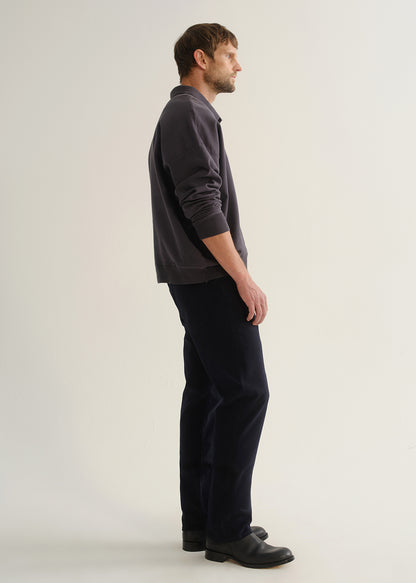Person wearing dark navy straight leg jeans with a charcoal long sleeve shirt and black boots, side full body view on a light grey background.