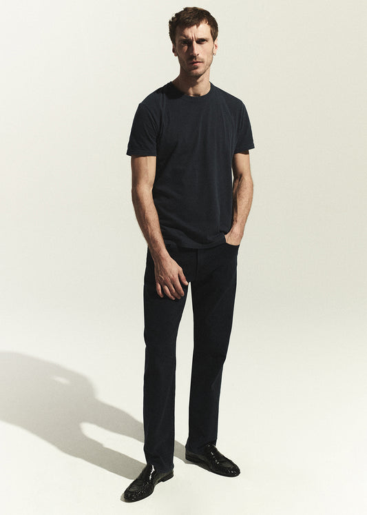Man wearing a navy t-shirt and dark navy jeans on a white background