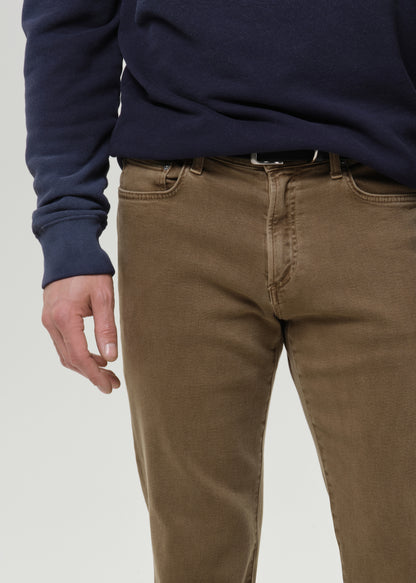 A close-up of a person wearing brown slim-fit jeans and a navy blue sweatshirt, cropped from the chest down against a grey background.