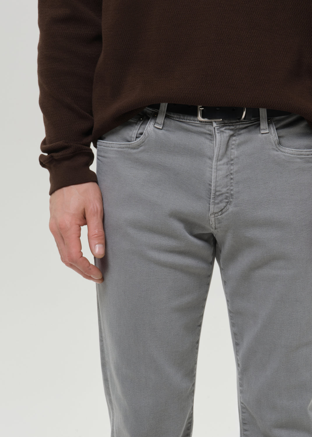 Person wearing grey pants and a brown sweater on a grey background