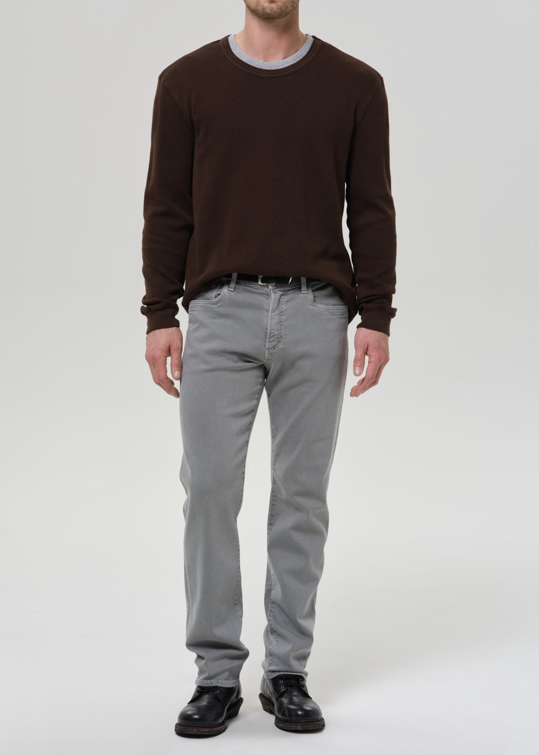 Person wearing a brown sweater and grey pants on a grey background