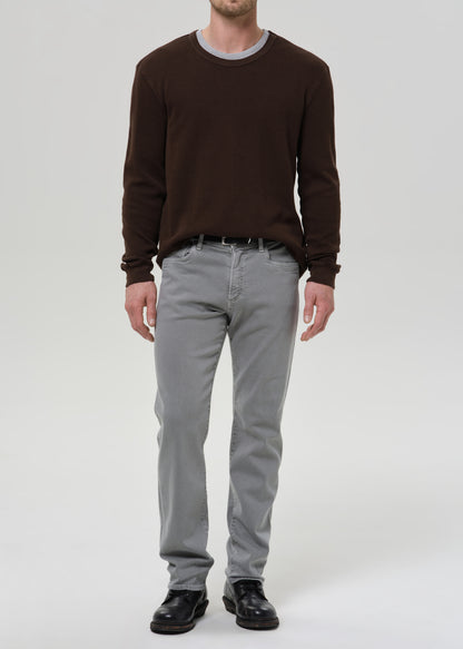 Person wearing a brown sweater and grey pants on a grey background