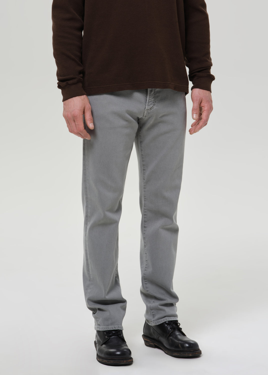 Person wearing grey pants and a brown jacket on a grey background