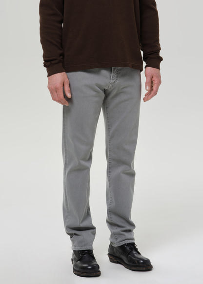 Person wearing grey pants and a brown jacket on a grey background