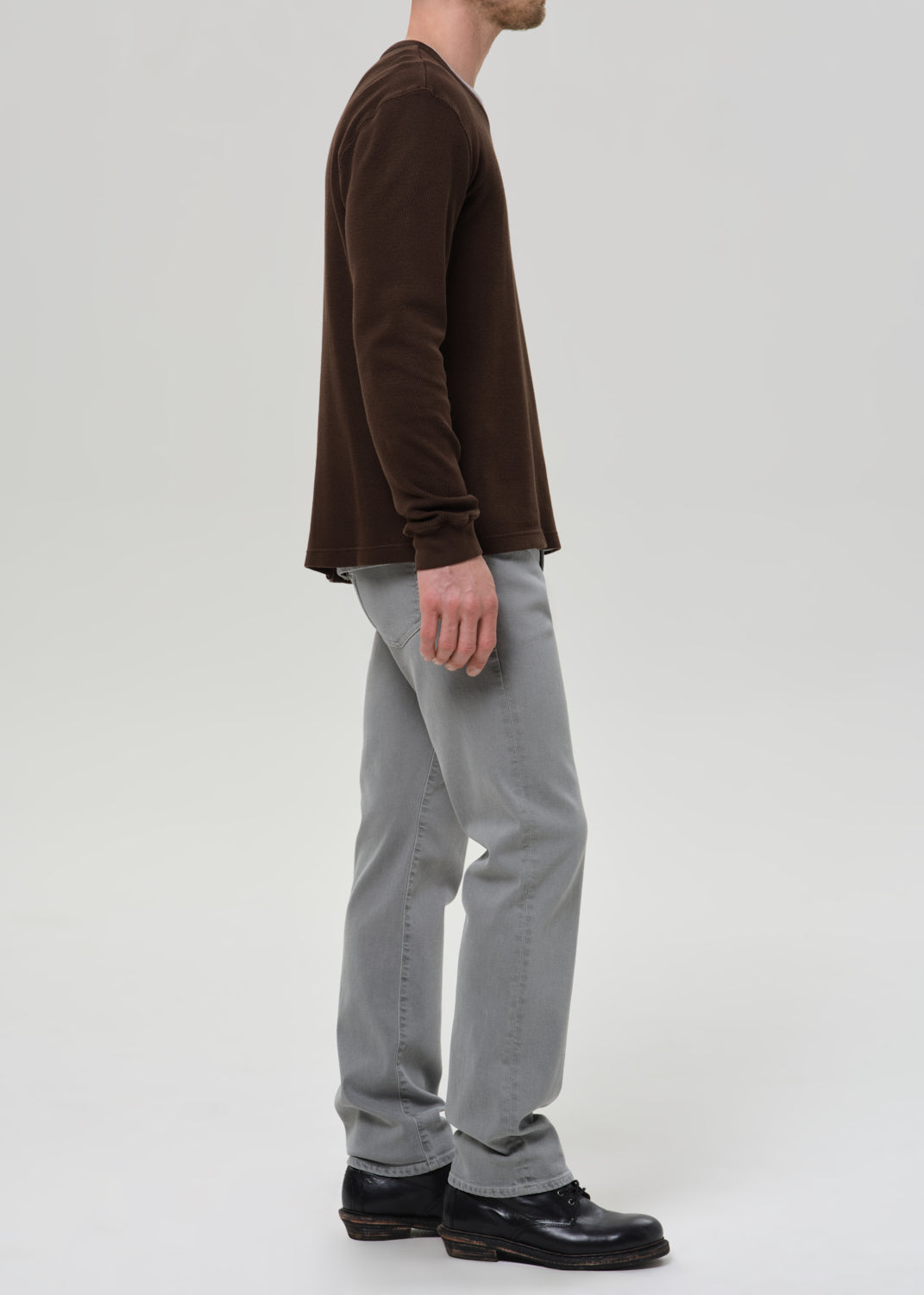 Person wearing a brown long-sleeve shirt and grey pants on a grey background