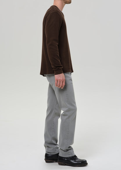 Person wearing a brown long-sleeve shirt and grey pants on a grey background