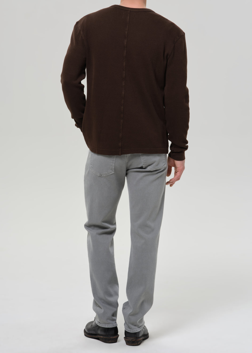 Person wearing a brown long-sleeve shirt and grey pants on a grey background