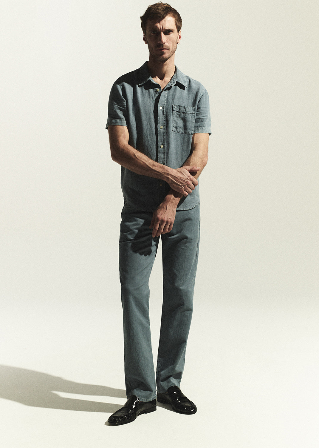 Man wearing a blue shirt and jeans standing against a white background