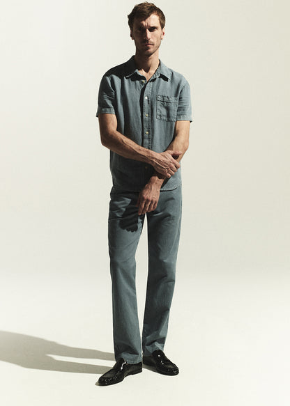Man wearing a blue shirt and jeans standing against a white background