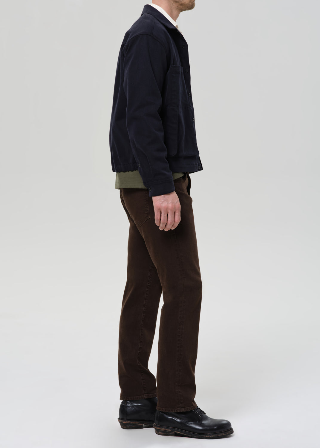 Man wearing a dark jacket, brown pants, and black shoes on a grey background