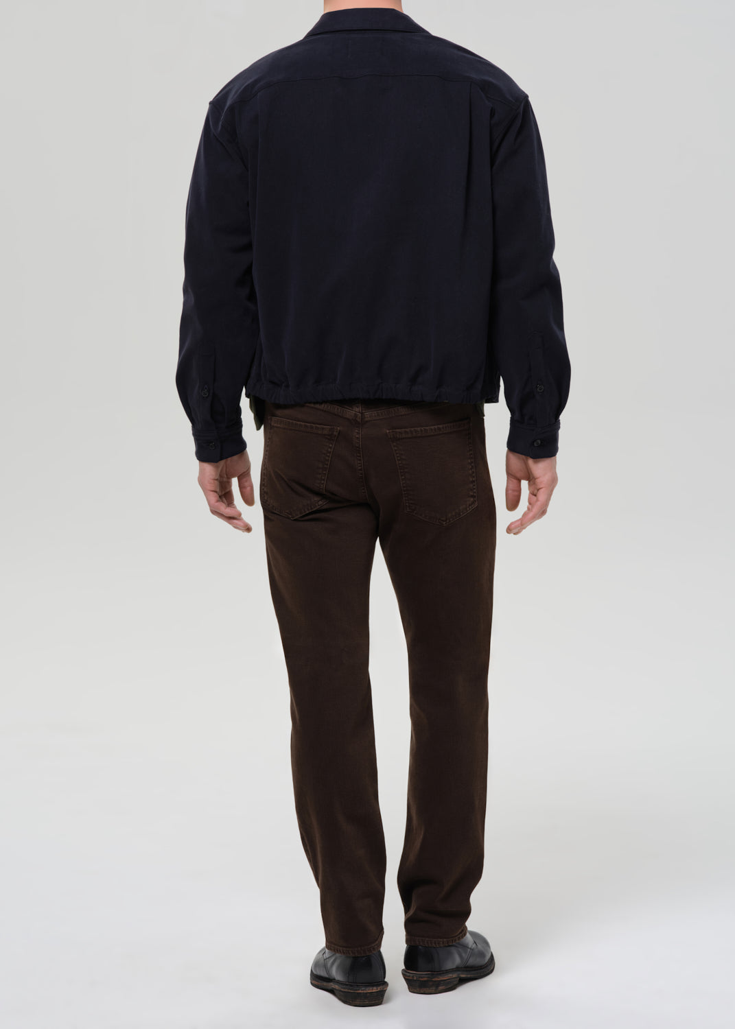 Person wearing a navy jacket and brown pants on a grey background