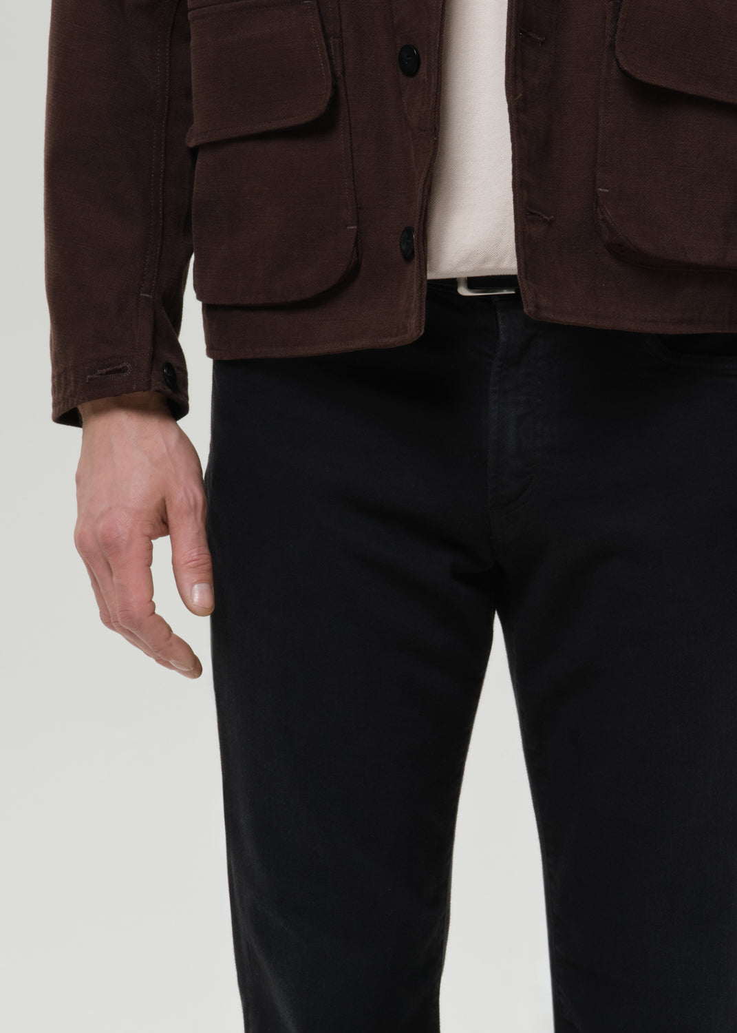 Person wearing a brown jacket and black pants on a grey background
