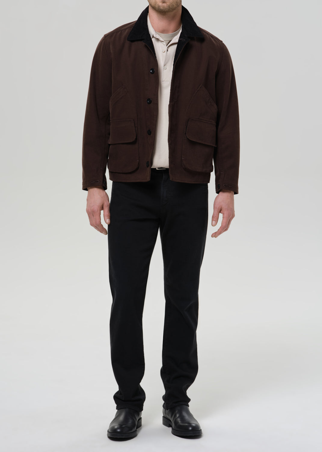 Man wearing a brown jacket and black pants on a grey background