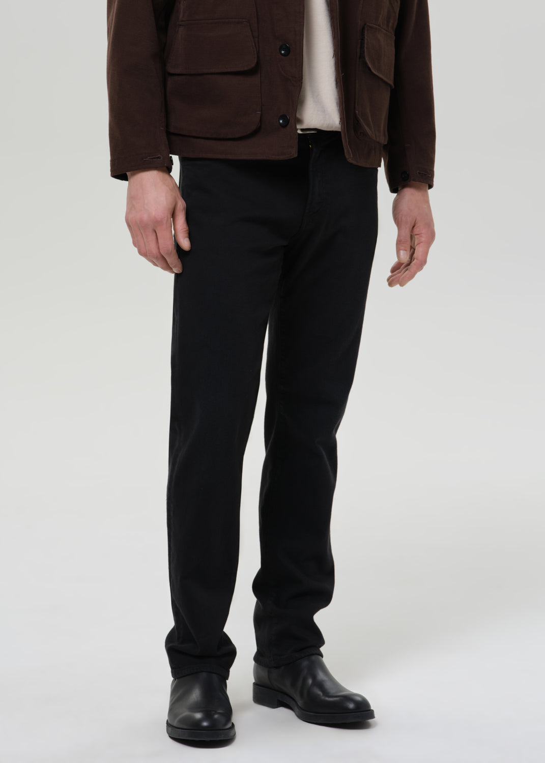 Person wearing a brown jacket, black pants, and black shoes on a grey background
