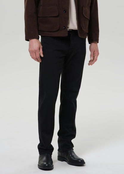Person wearing a brown jacket, black pants, and black shoes on a grey background