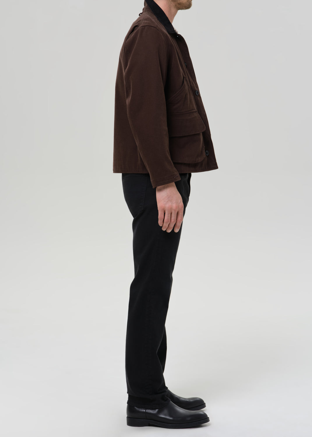 Person wearing a brown jacket and black pants on a grey background
