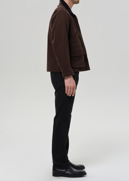Person wearing a brown jacket and black pants on a grey background