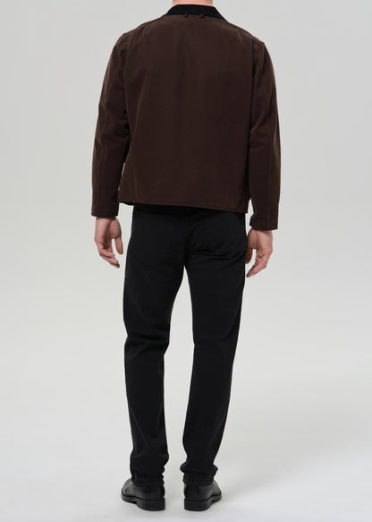 Person wearing a brown jacket and black pants on a grey background