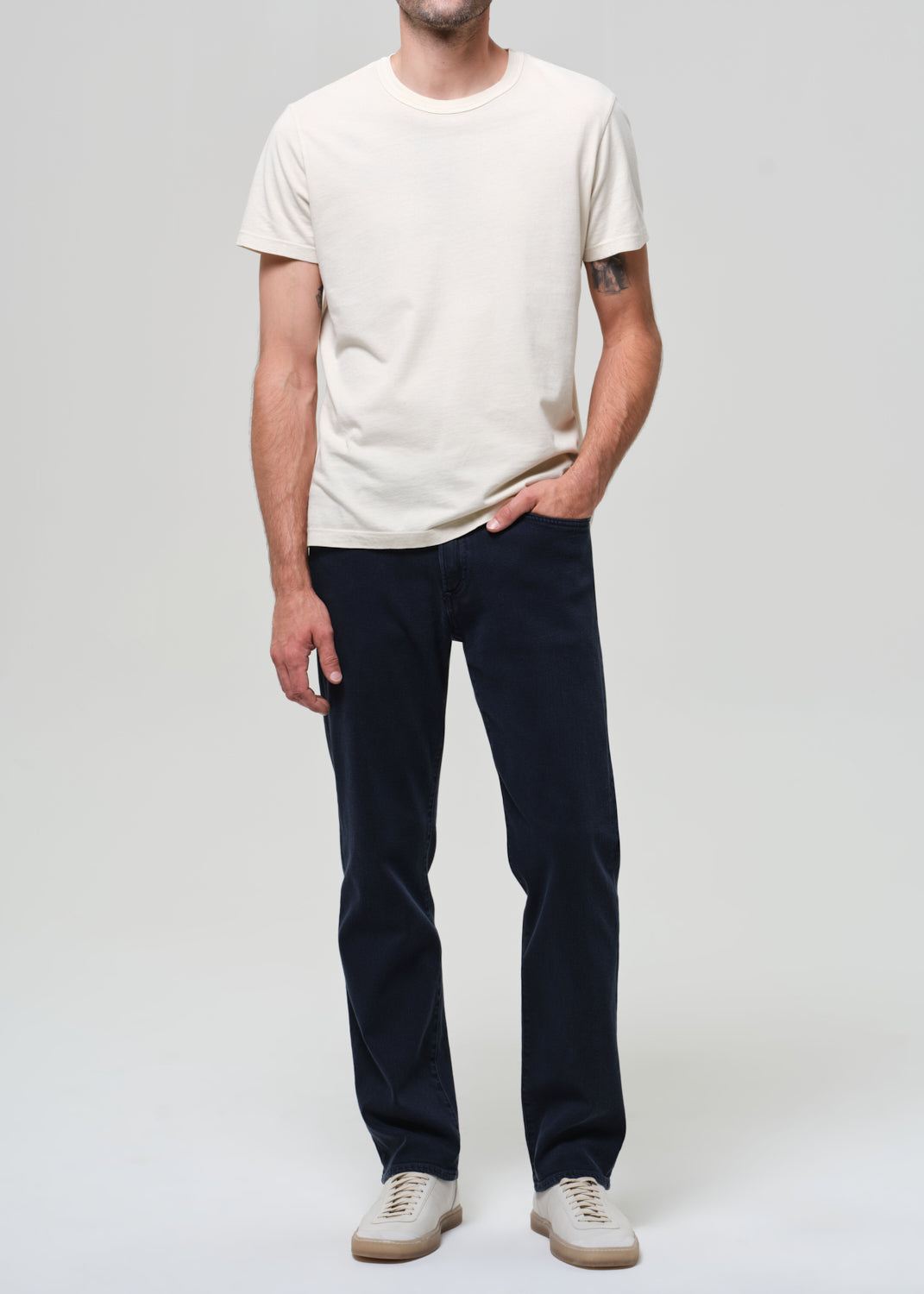 Man wearing a white t-shirt and dark pants on a plain background