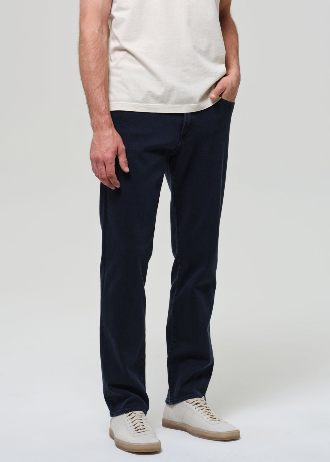 Person wearing navy pants and a white shirt on a plain background
