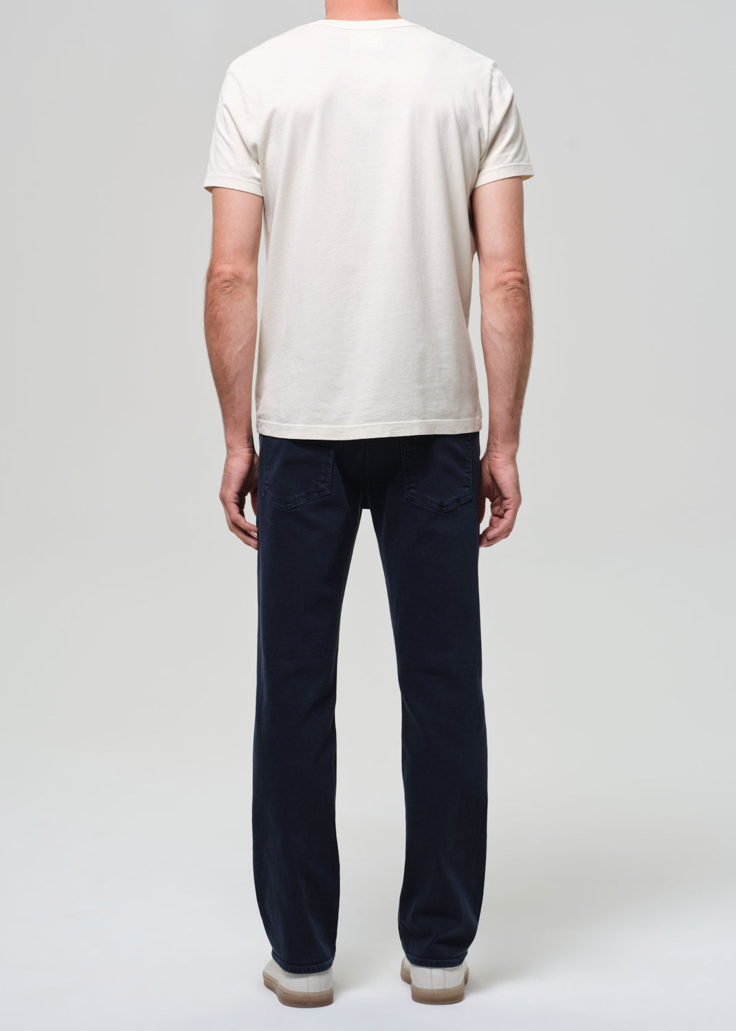 Person wearing a white t-shirt and dark blue jeans on a plain background