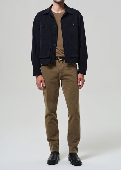 Person wearing a black jacket, beige shirt, and brown pants on a white background