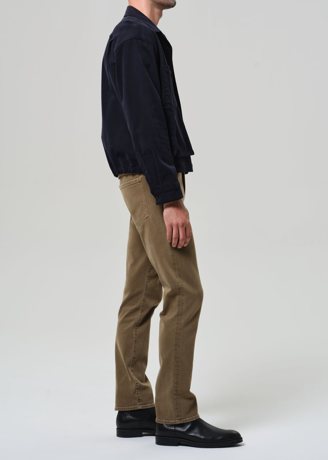 Person wearing a navy jacket and brown pants on a white background