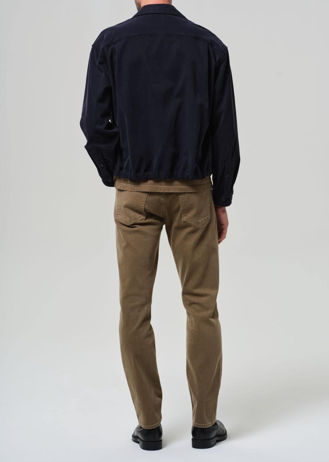 Person wearing a navy jacket and brown pants on a white background