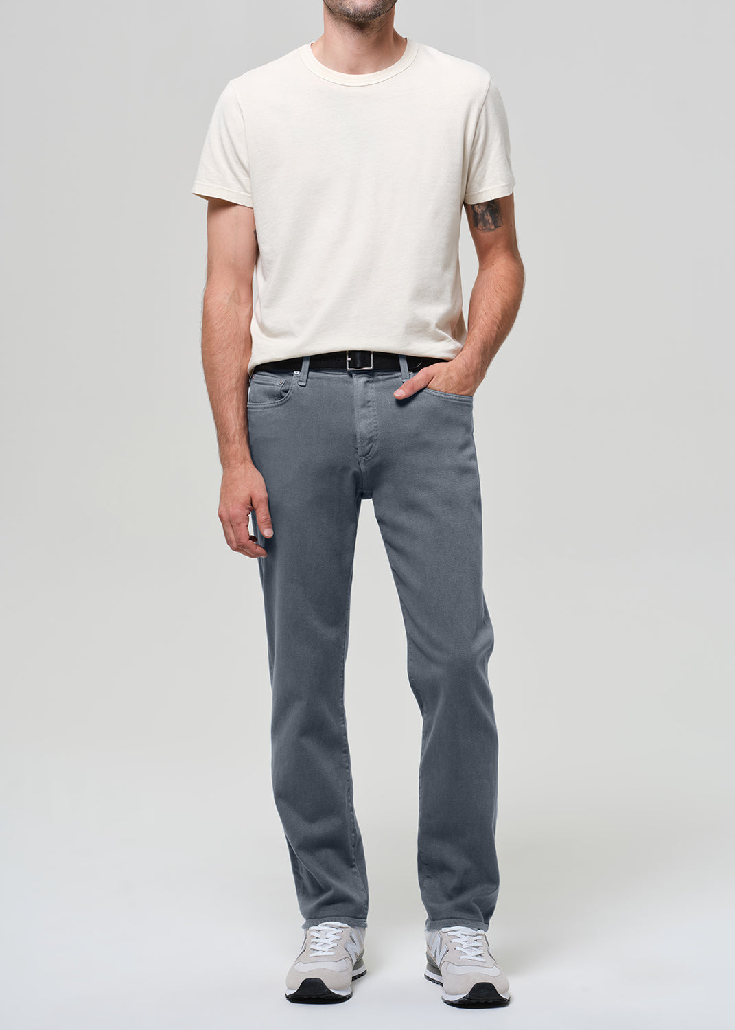 Person wearing a white shirt, grayish blue jeans, and sneakers on a plain background