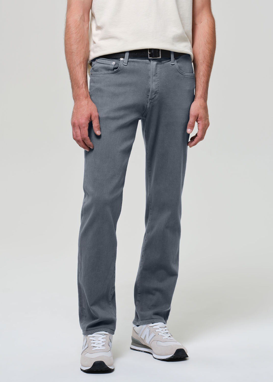 Person wearing a white shirt, grayish blue jeans, and sneakers on a plain background
