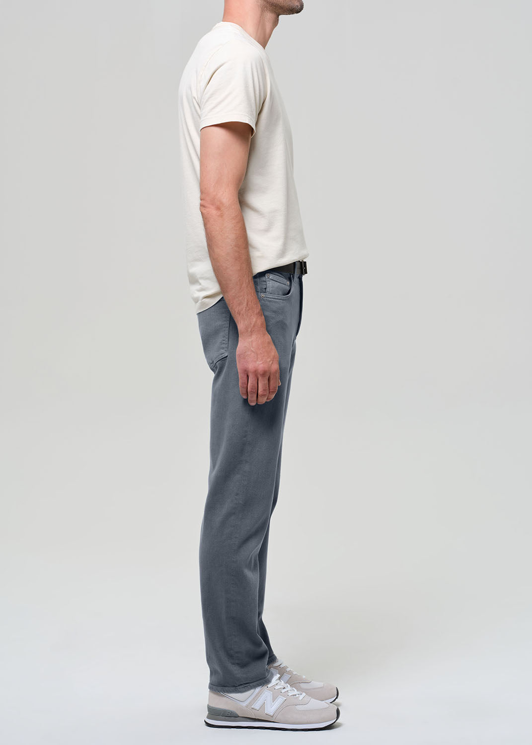 Person wearing a white shirt, grayish blue jeans, and sneakers on a plain background