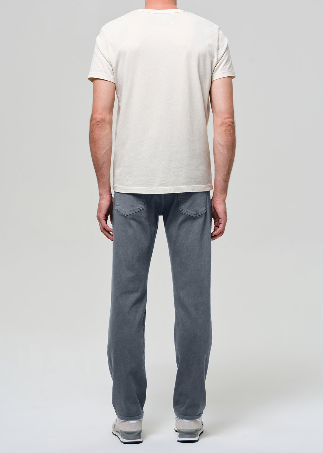 Person wearing a white shirt, grayish blue jeans, and sneakers on a plain background