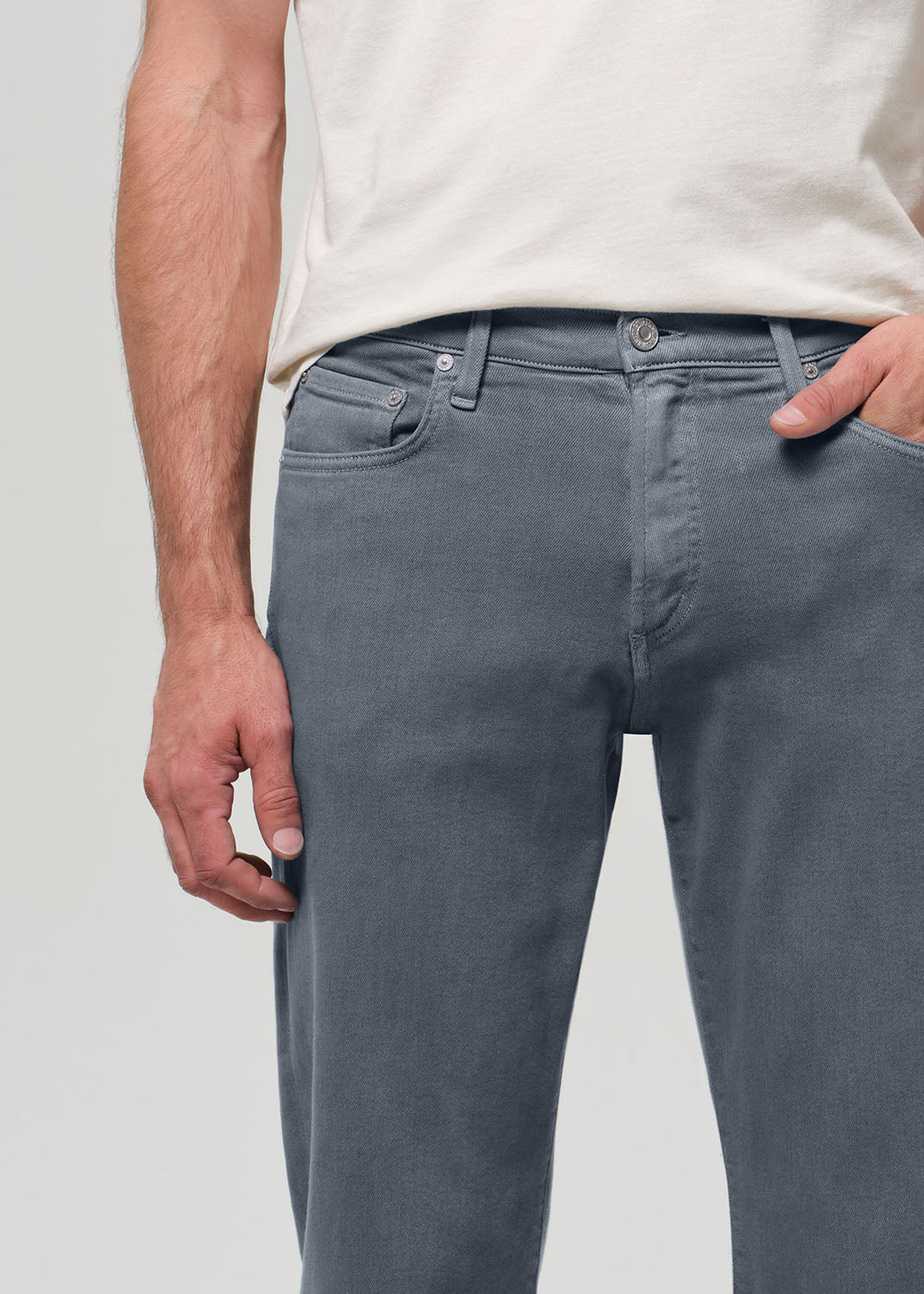 Person wearing a white shirt, grayish blue jeans, and sneakers on a plain background