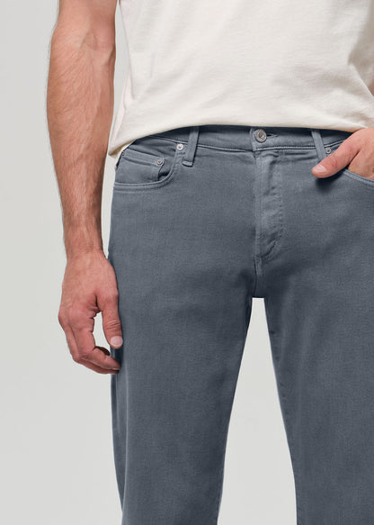 Person wearing a white shirt, grayish blue jeans, and sneakers on a plain background