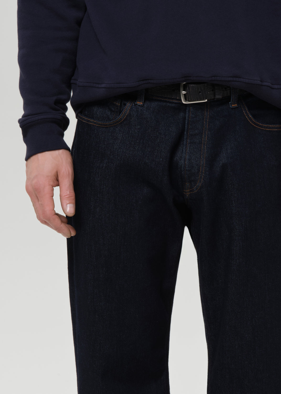 Person wearing dark blue jeans and a navy sweater on a grey background