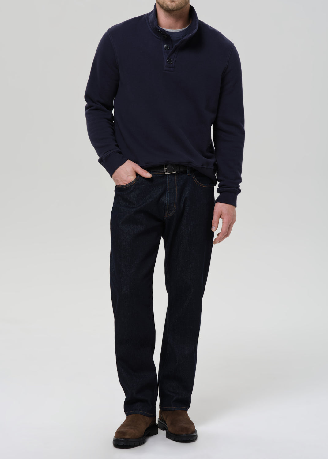 Person wearing a navy sweater and dark pants on a grey background