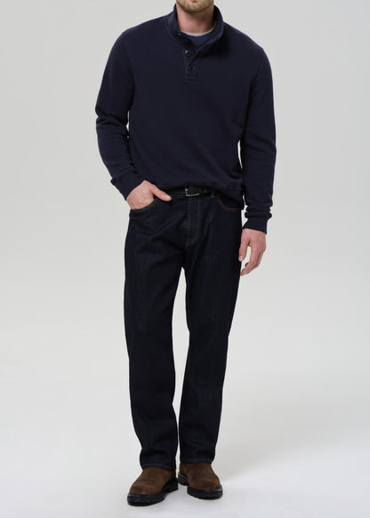 Person wearing a navy sweater and dark pants on a grey background