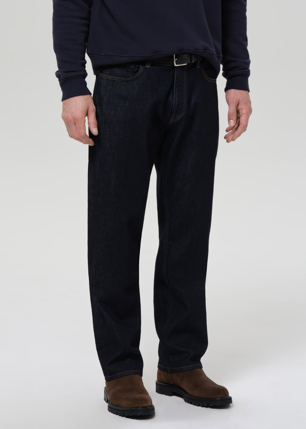 Person wearing dark blue jeans and a dark shirt on a grey background